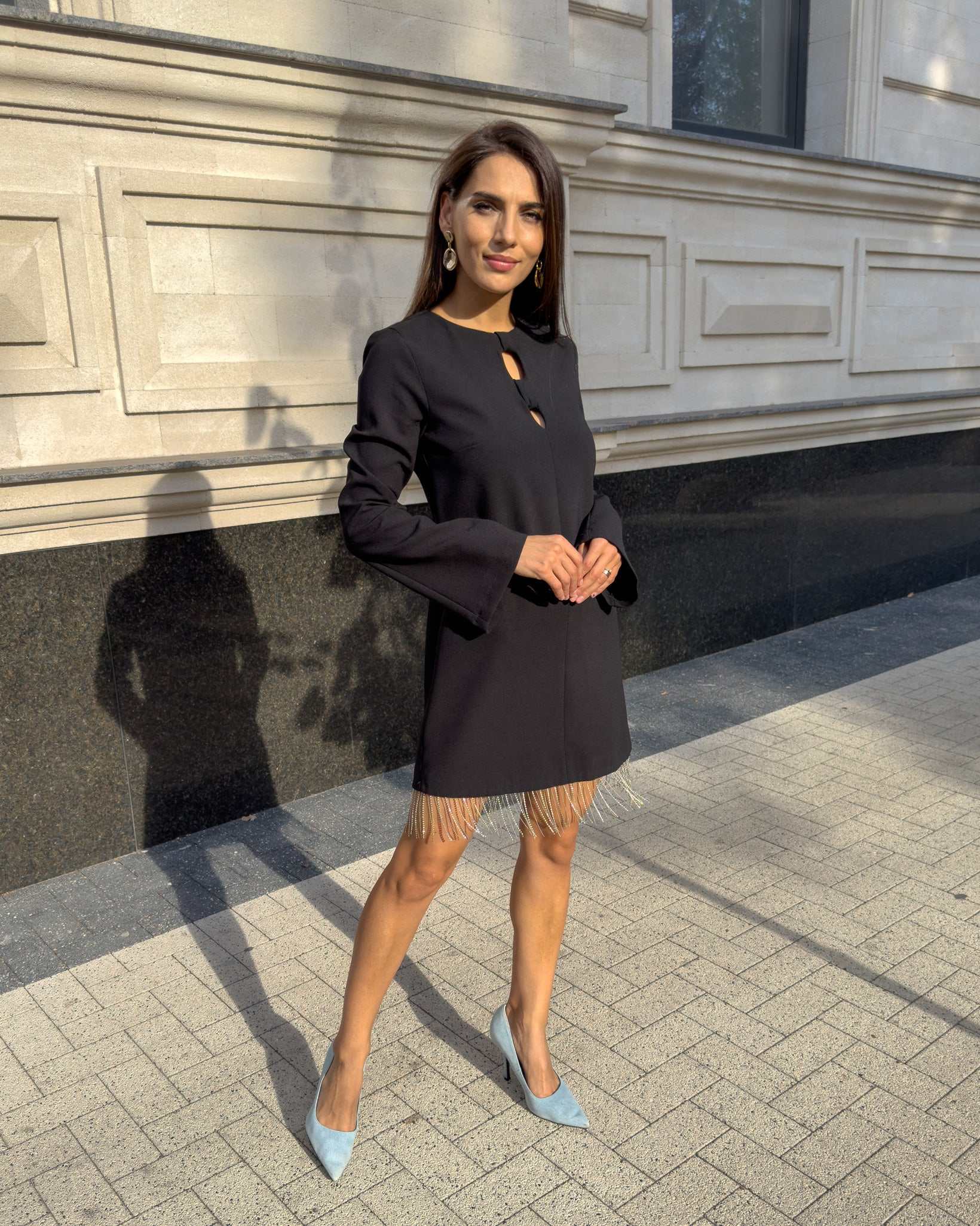 Rochie neagra scurtă cu franjuri din cristale și mâneci lungi, în fundal urban.