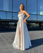 Rochie de mireasa albă lungă cu slit senzual și design elegant, potrivită pentru evenimente formale.