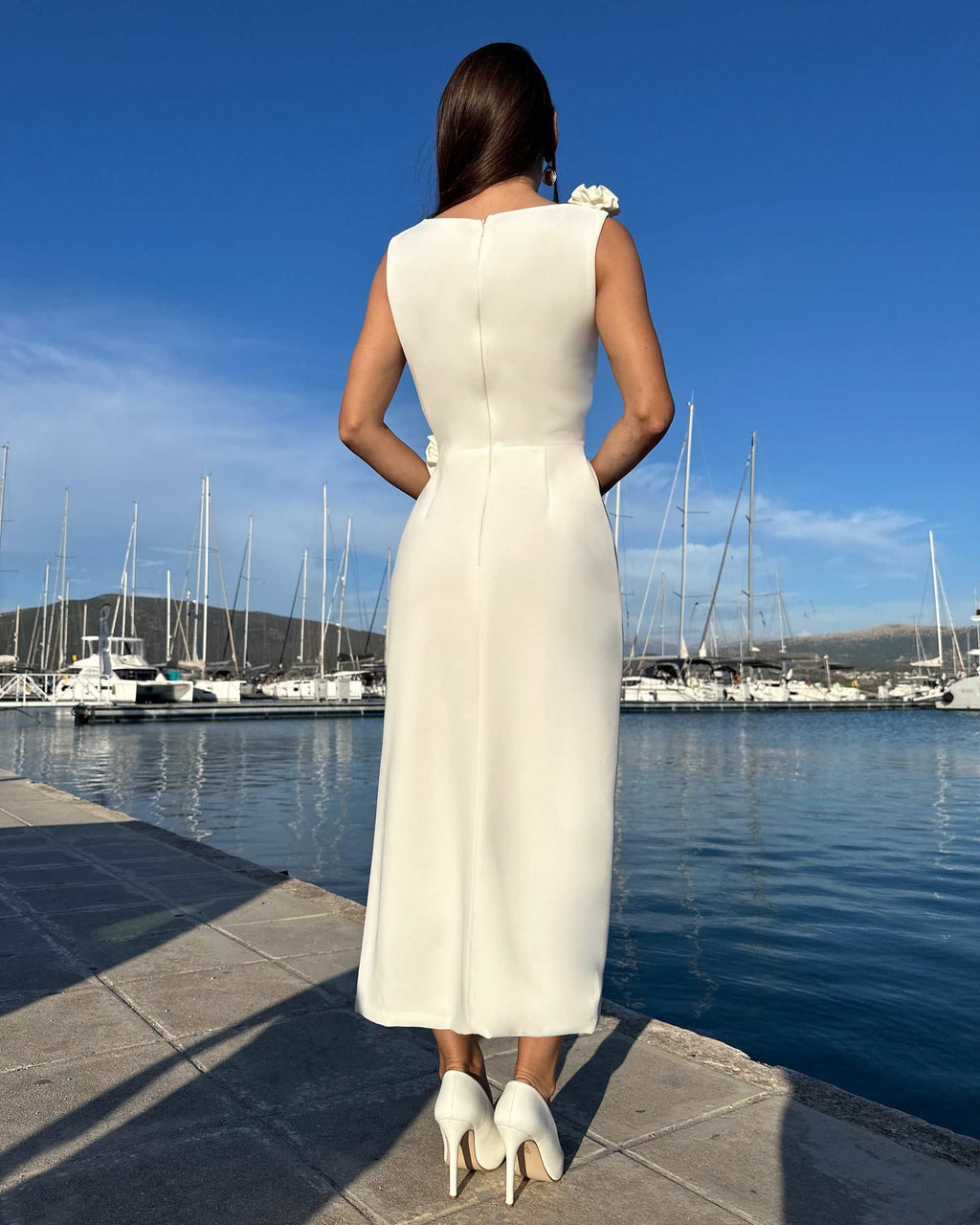 Rochie alba cu slit fără mâneci, detalii florale, fermoar discret, fundal marin.
