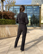 Bluza dama neagra cu guler și detaliu decorativ la bust, purtată de model în picioare, vedere din spate.