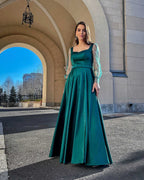 Rochie lunga verde smarald din satin cu mâneci transparente, decolteu pătrat și design elegant.