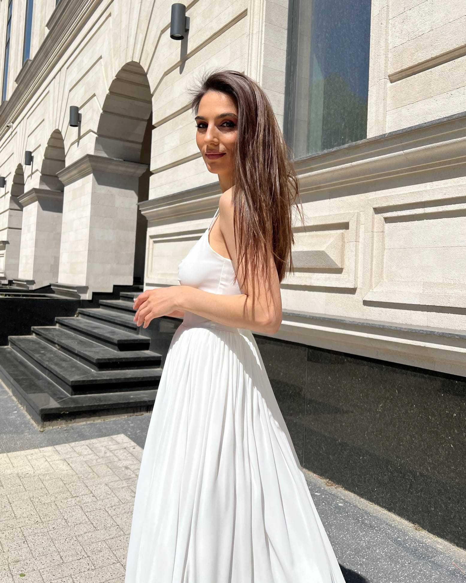 Rochie alba elegantă cu bretele și slit, accesorizată cu centură.